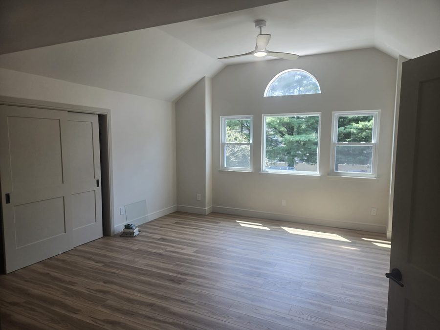 Freshly painted bedroom with vaulted ceiling, ceiling fan, and arched window