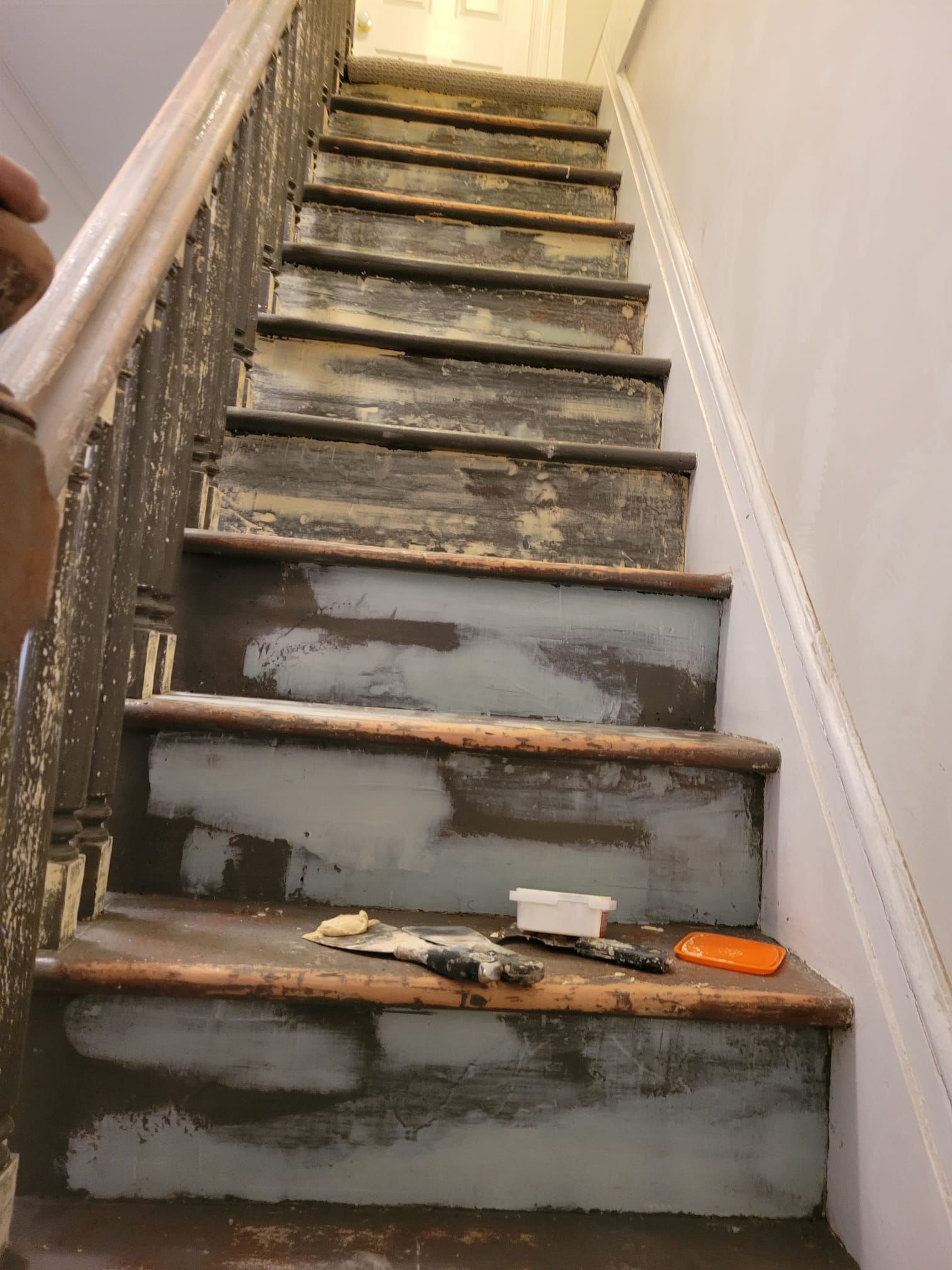 Before: worn, chipped staircase with stripped wooden treads mid-refinish